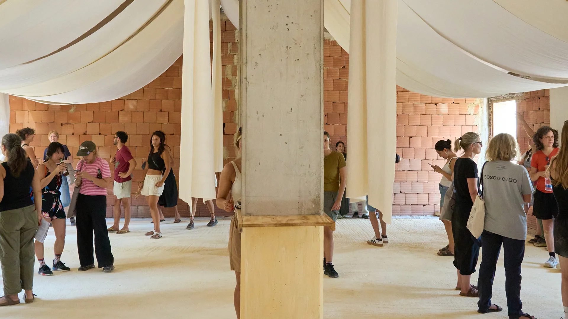 Interno con persone e colonna in legno — BC26, Bosco di Santo Pietro, luglio–agosto 2026